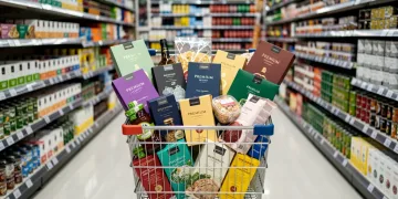 Shopping cart filled with premium store brand groceries in a modern supermarket aisle.